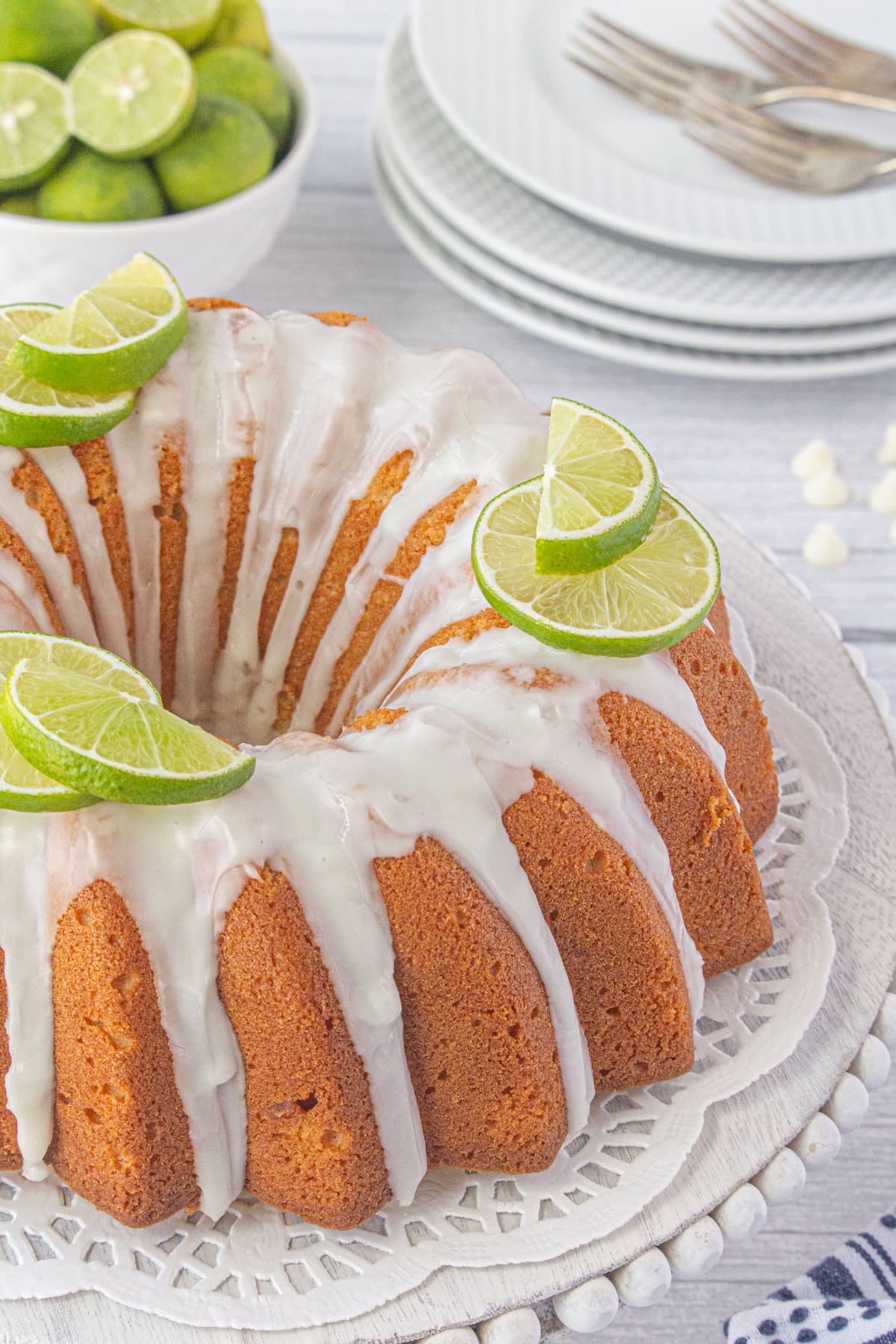 A white chocolate key lime bundt cake on a serving platter garnished with lime slices.