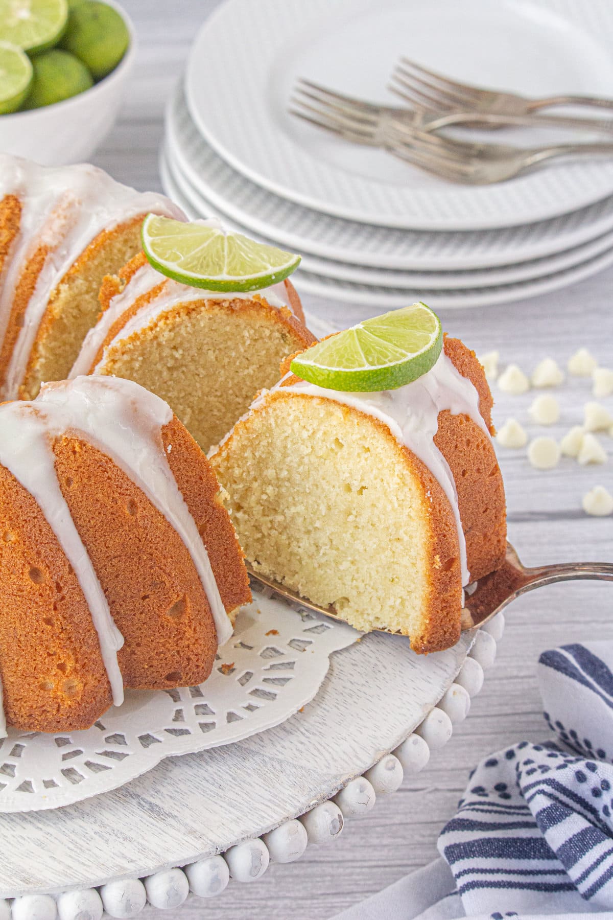 A slice of white chocolate key lime bundt cake on a cake server hovered near the rest of the cake.