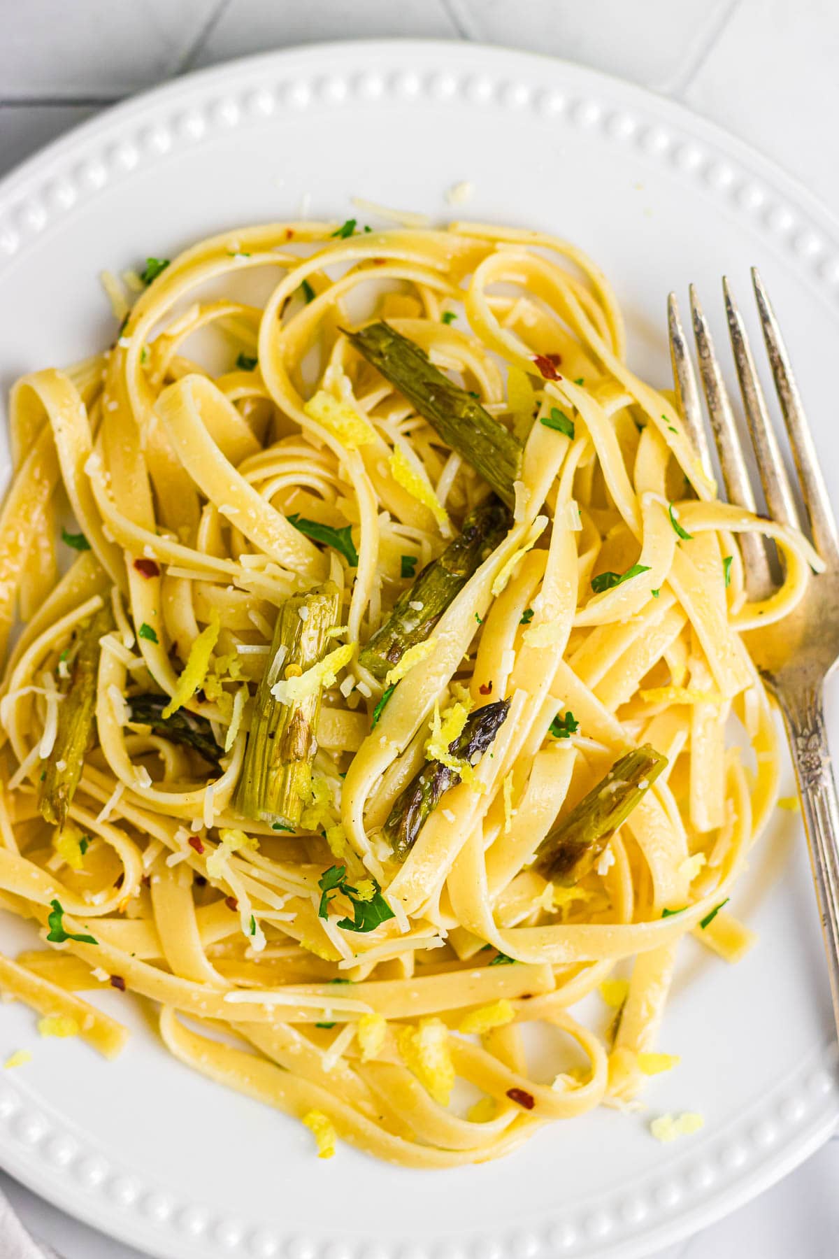Pasta with asparagus, zest, and herbs on a white plate.