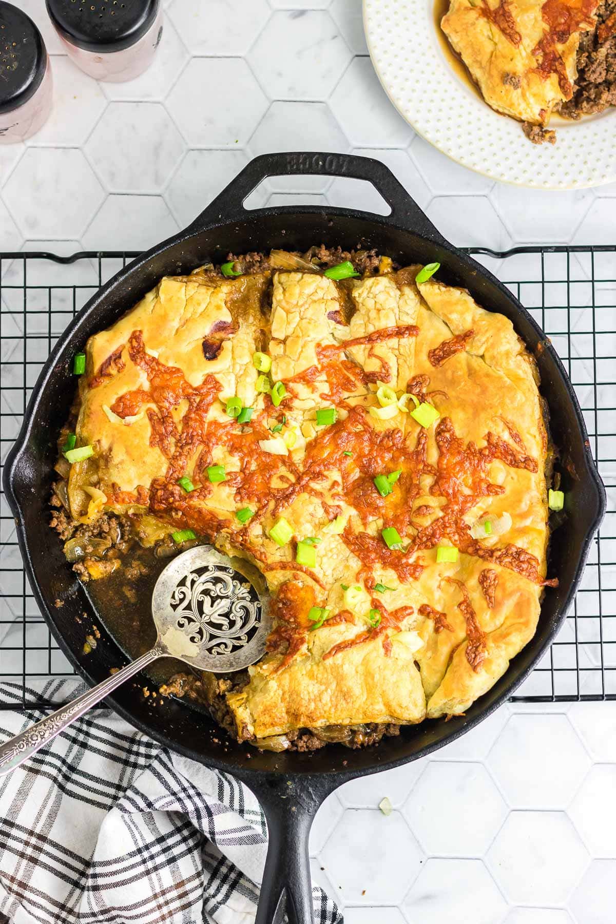 Puff pastry cheeseburger pot pie in a skillet with one scoop removed.
