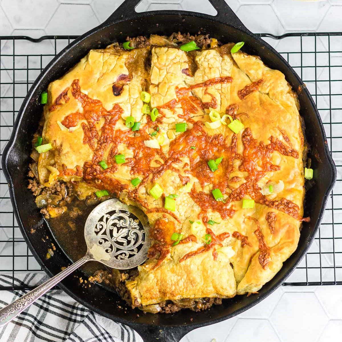 Overhead view of a cast iron skillet with a finished cheeseburger pot pie inside.