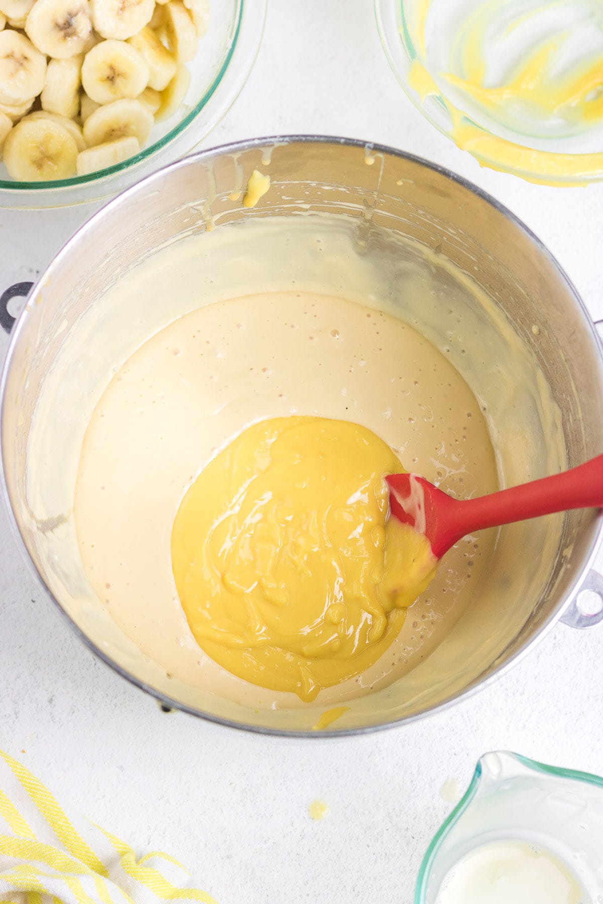 Pudding mixture, beaten cream cheese, and condensed milk being stirred together.
