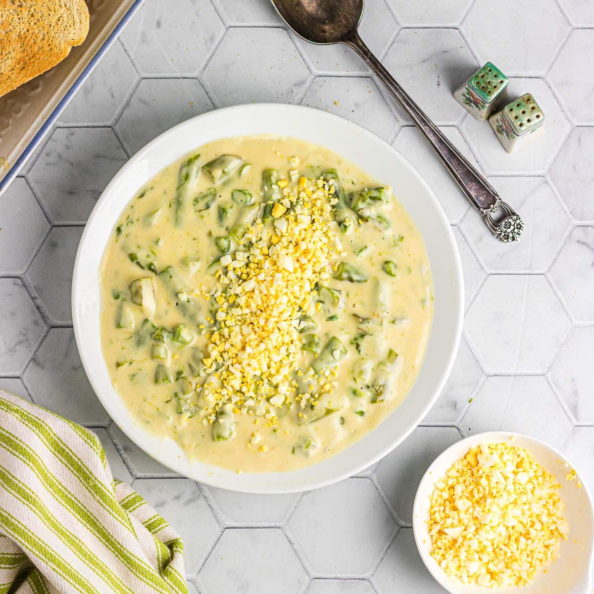 Overhead view of a bowl of creamed asparagus on a tile countertop.