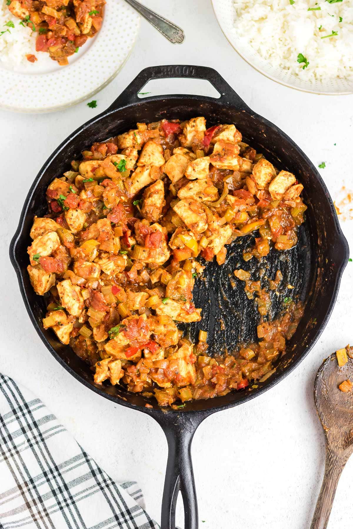 Creole chicken in a skillet, with some removed to a plate with rice on the side.