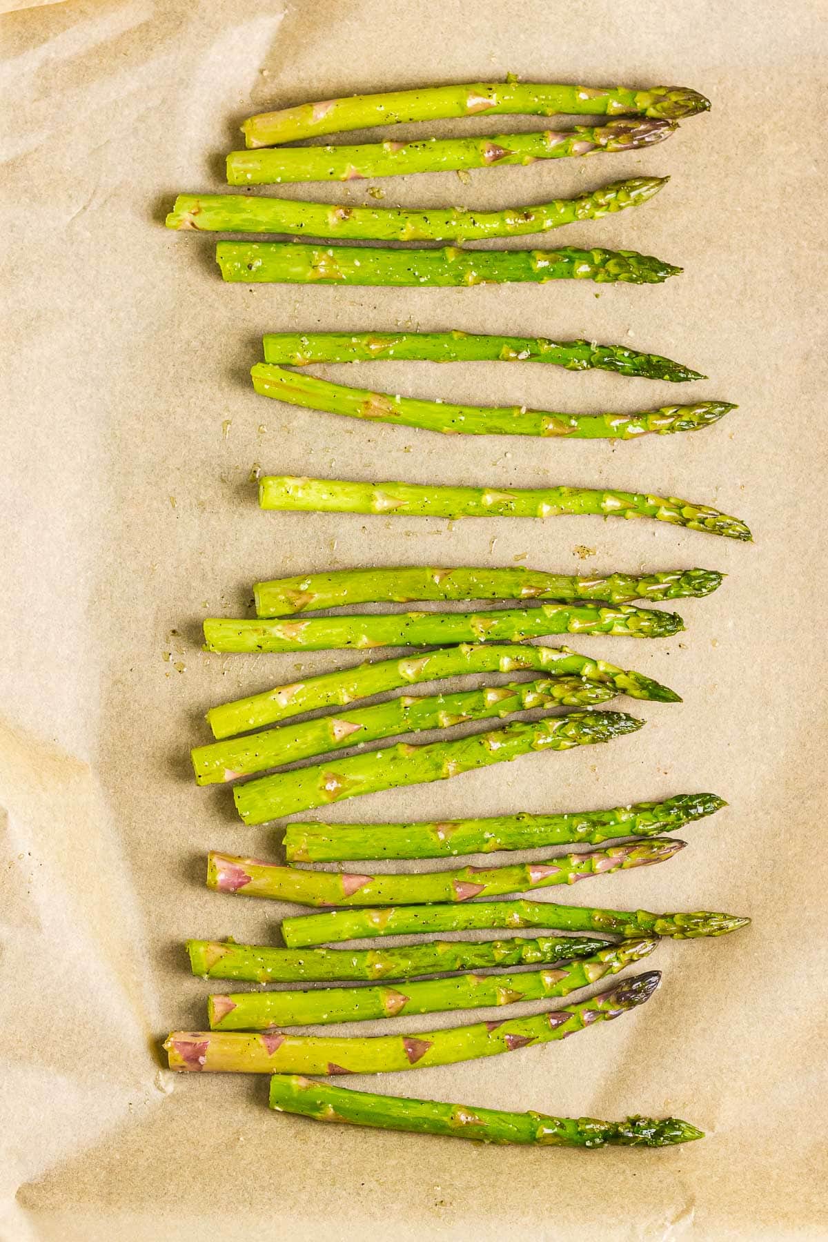 Seasoned asparagus spears on a parchment paper-lined baking sheet.