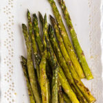 Overhead view of roasted asparagus on a white plate.