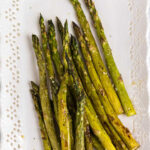 Overhead view of roasted asparagus on a white plate.