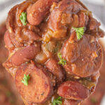 Over head view of a ladle full of red beans and rice being removed from the pot with a title text overlay for Pinterest.