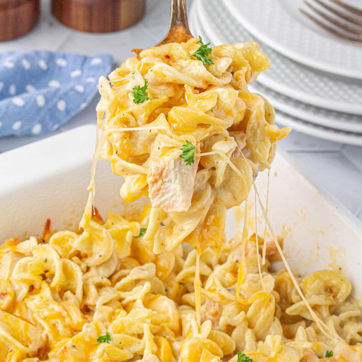 Creamy chicken and noodles being served from a white casserole dish.