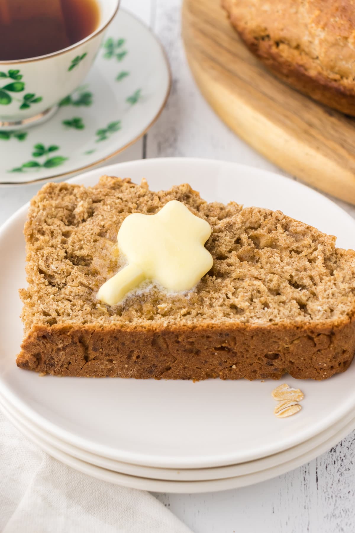 Closeup of a slice of Irish soda bread with a shamrock shaped pat of butter melting on top.
