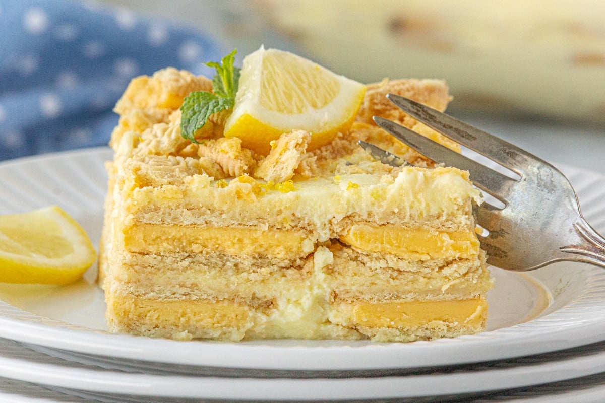 A slice of lemon icebox cake on a plate with a fork cutting into it.