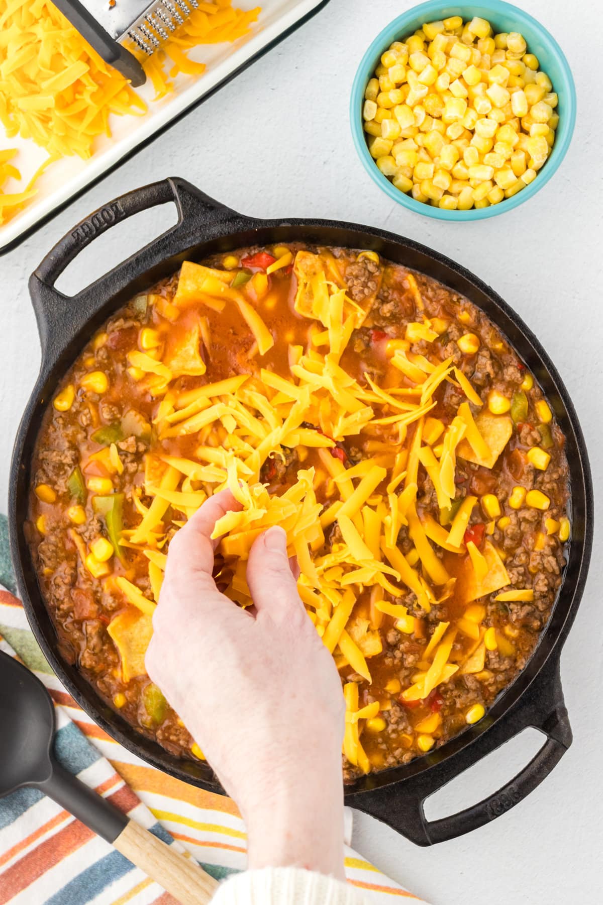 Sprinkling cheese over the cooked skillet beef tamale mixture.