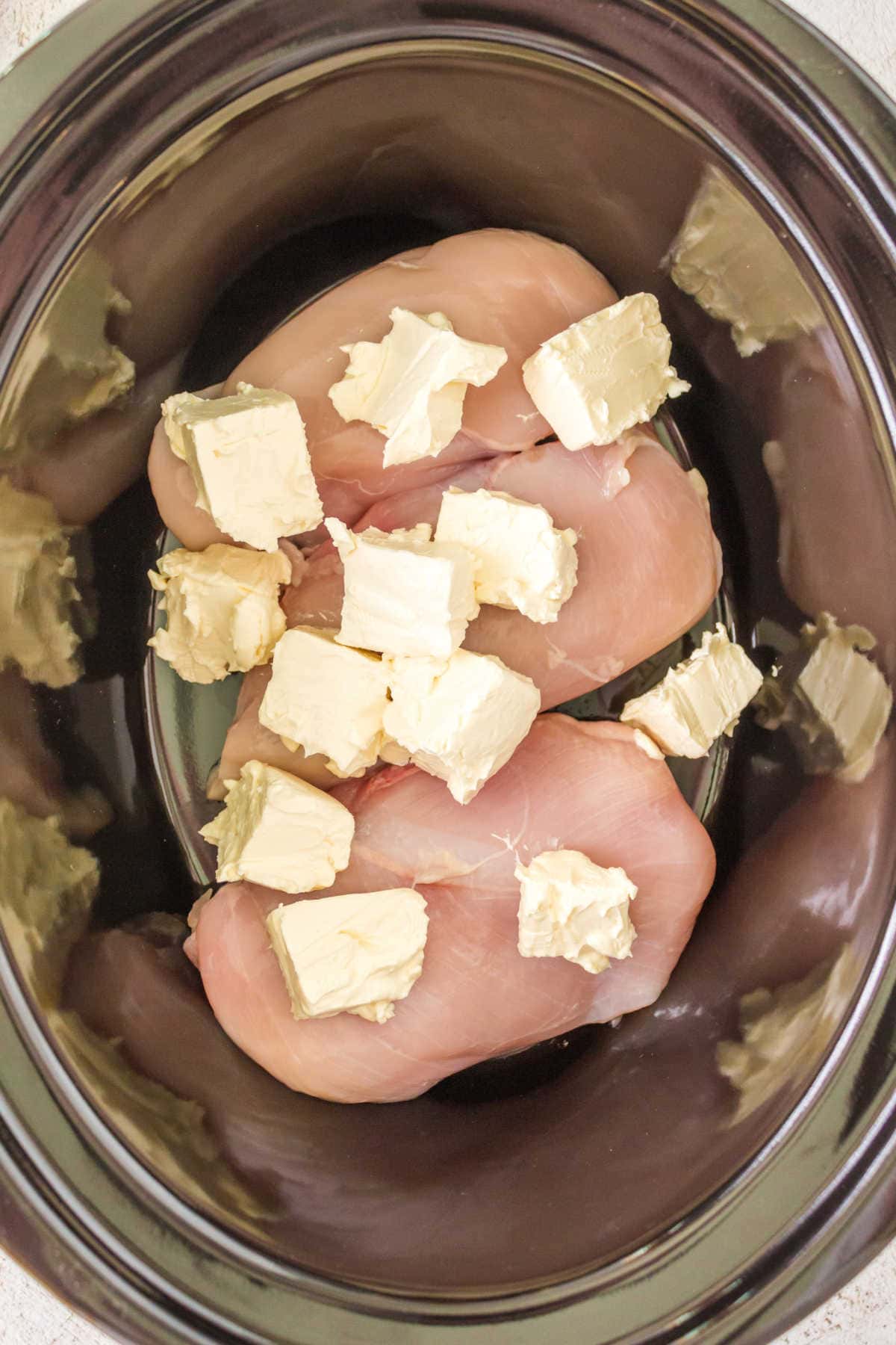Chicken breast in the slow cooker topped with cubed cream cheese.