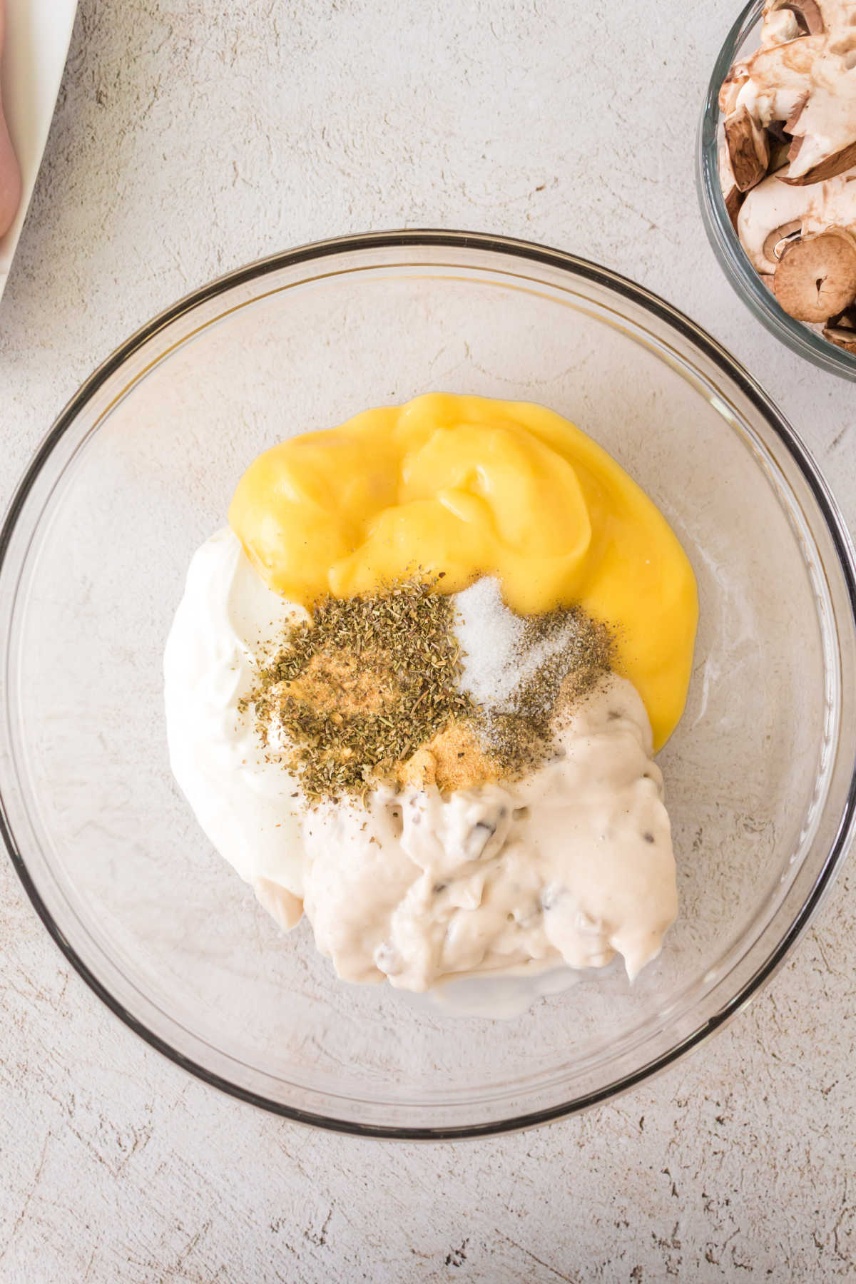 A mixture of sour cream, cream of chicken soup, cream of mushroom soup, and seasonings in a glass bowl.