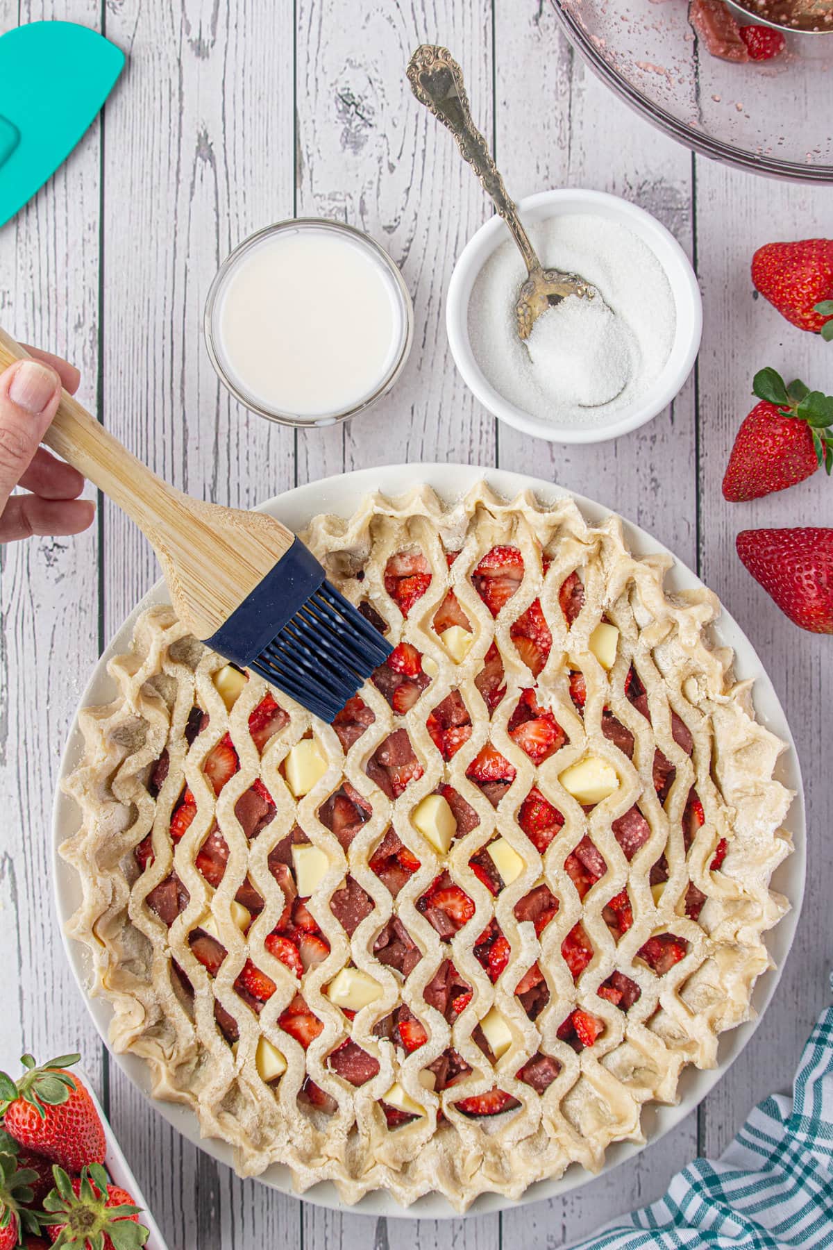 Lattice topped pie being brushed with milk.