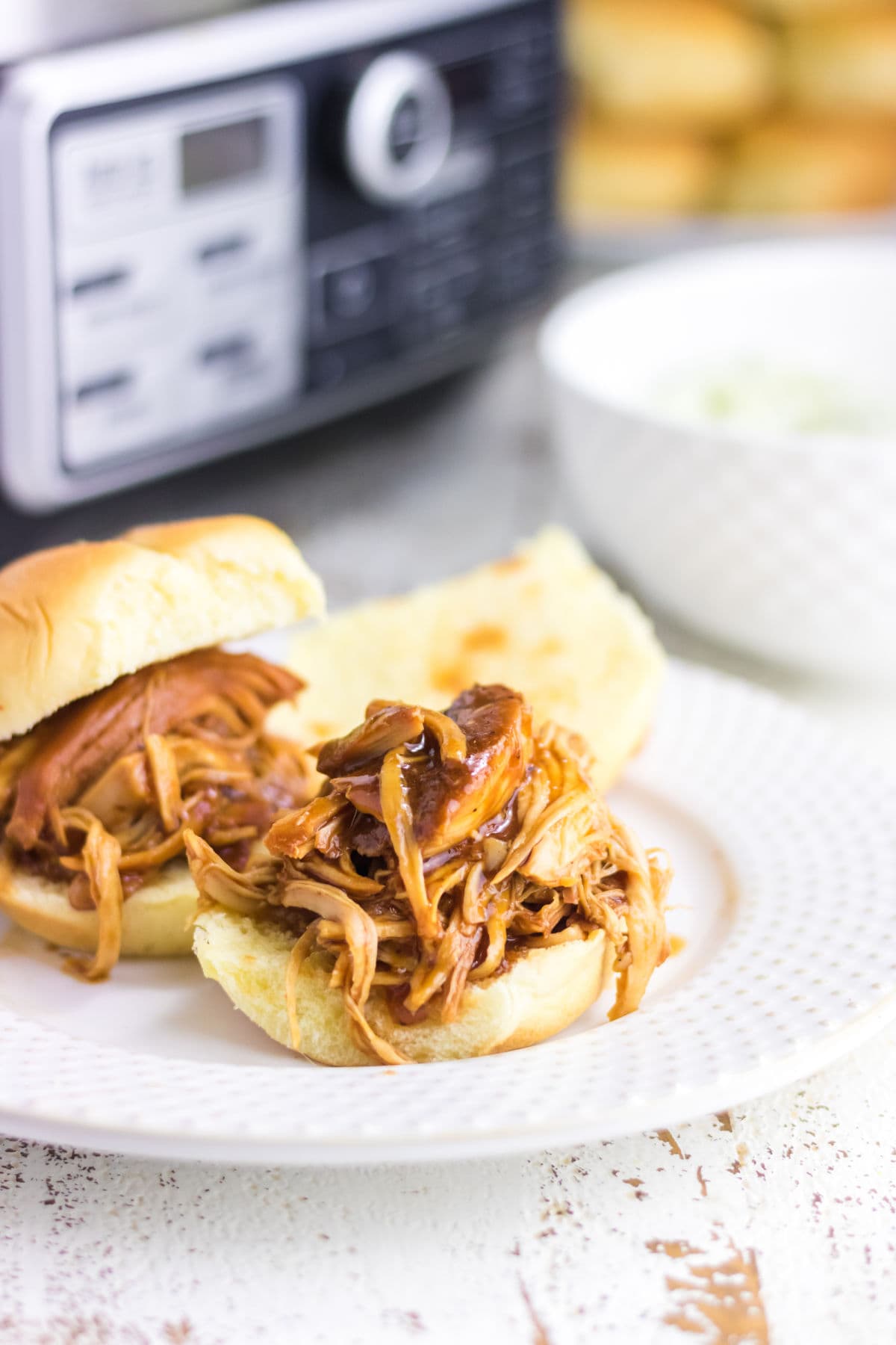 Closeup of shredded root beer chicken in a thick sauce spooned over a hamburger bun.