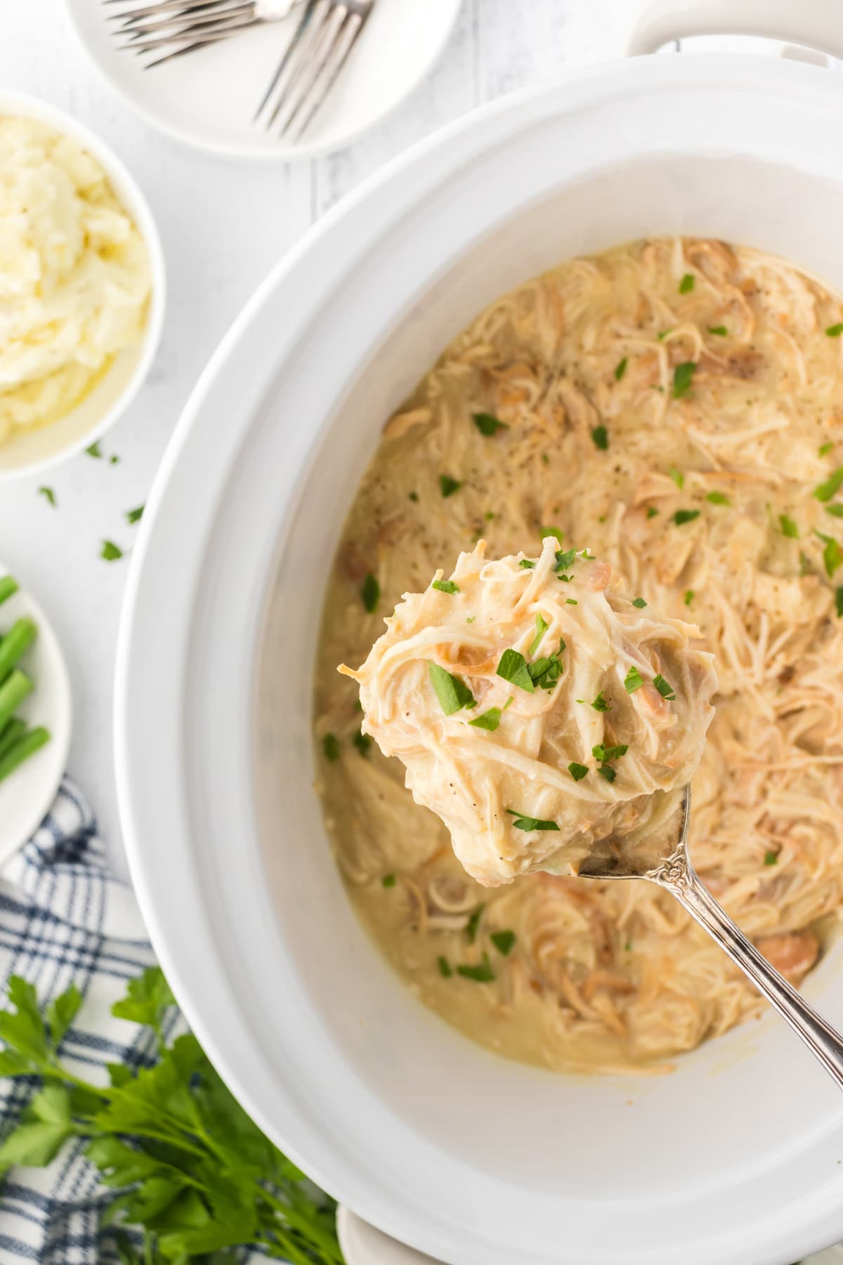 Overhead view of crockpot chicken and gravy being served out of a white crock.