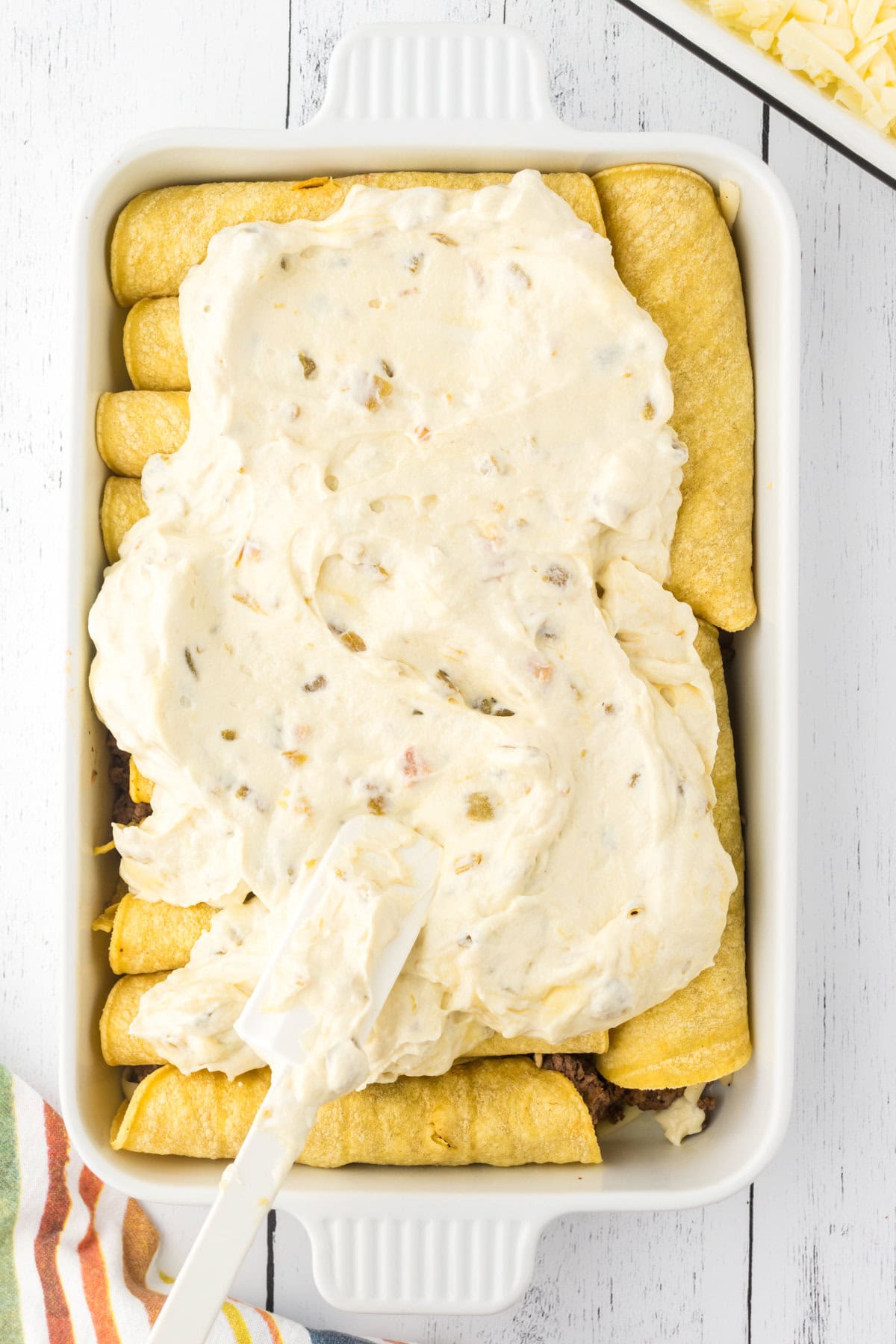 Spreading the enchilada sauce over the rolled enchiladas.