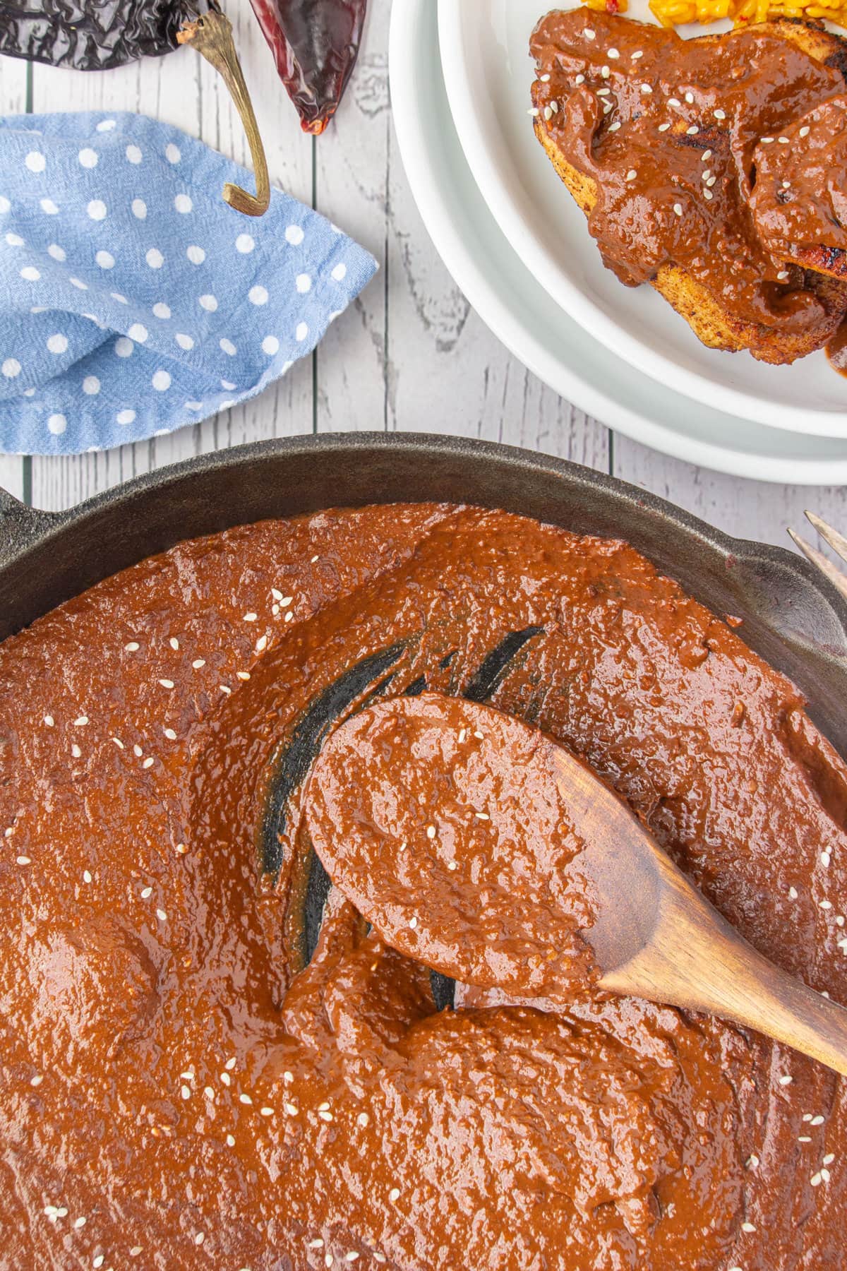 A wooden spoon lying in a skillet with leftover mole sauce in it.