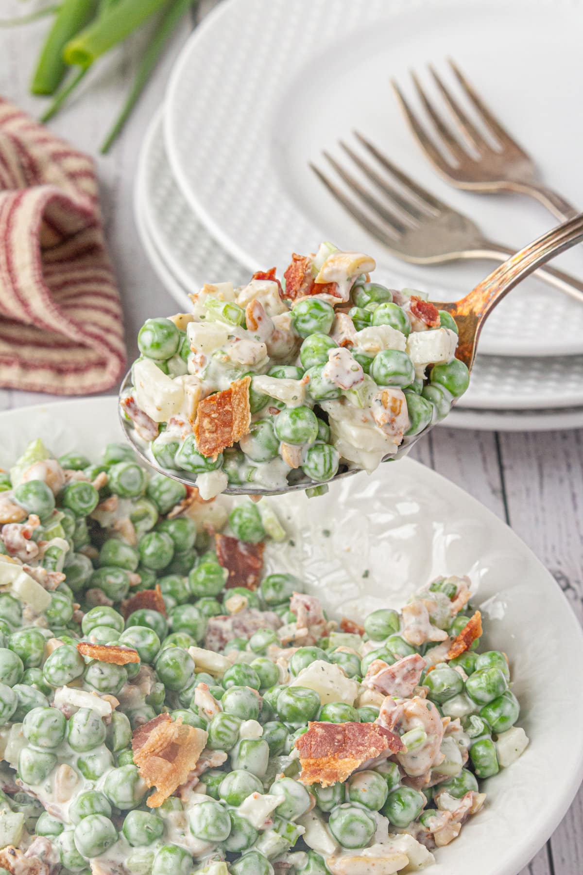 A spoonful of potluck pea salad with bacon hovered over the serving bowl.