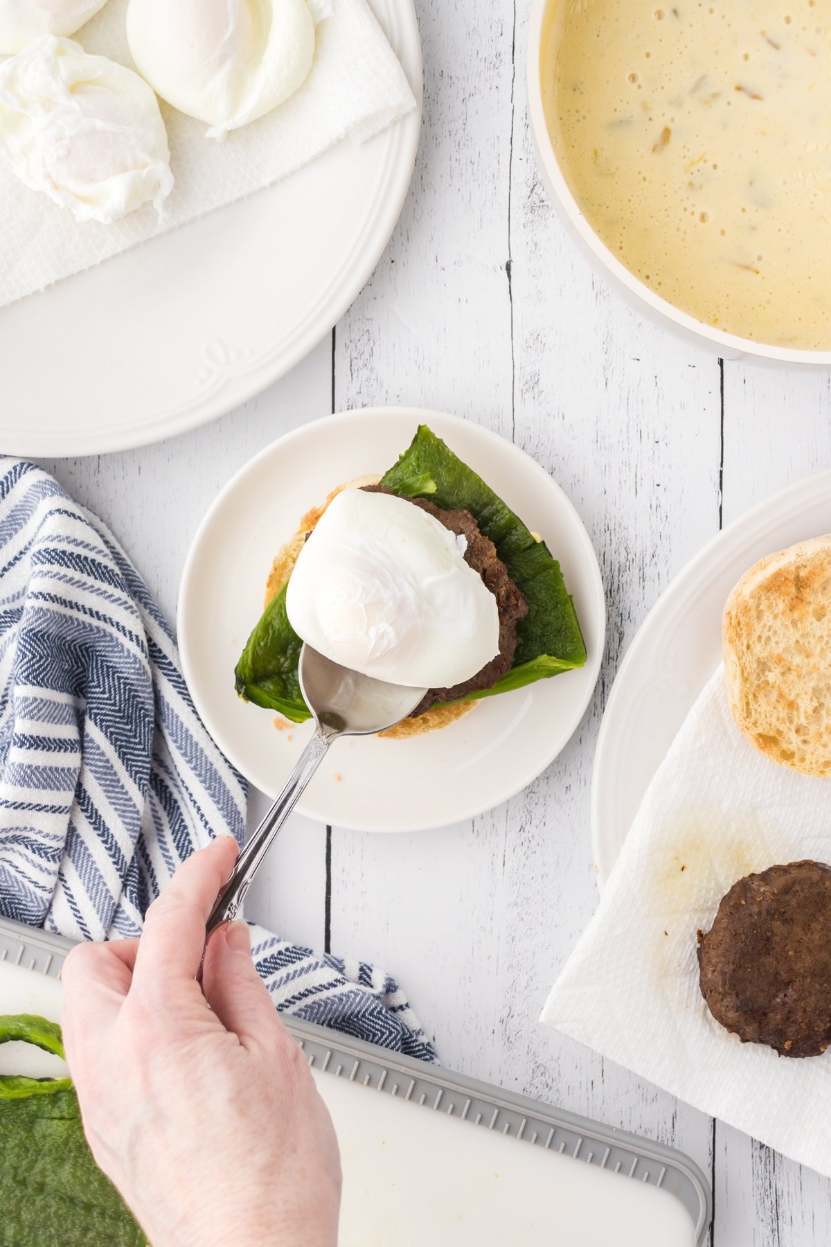 A poached egg is being lifted onto the sausage patty with a spoon.