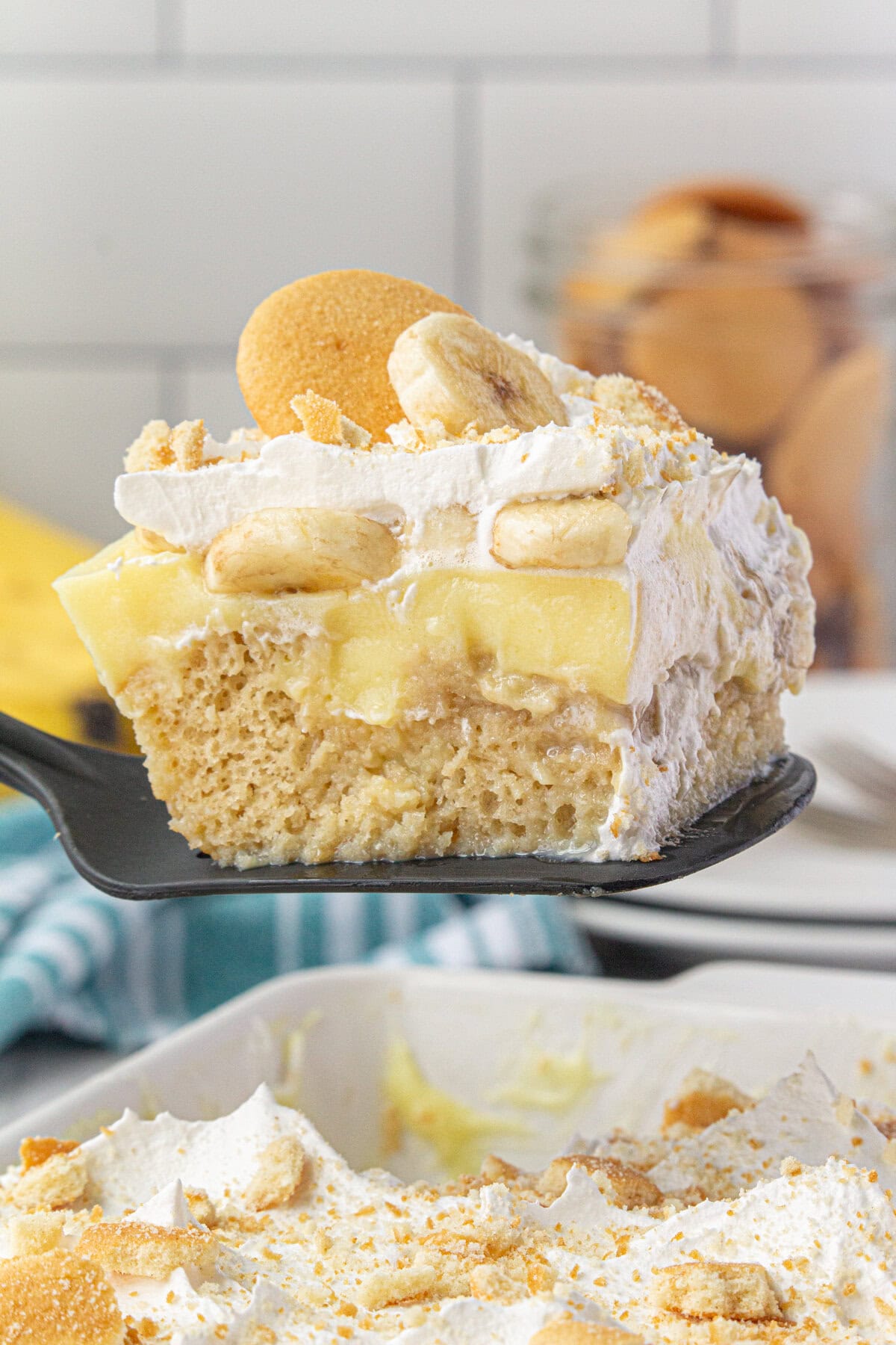 Banana pudding poke cake with bananas, creamy banana pudding, and whipped cream being served.