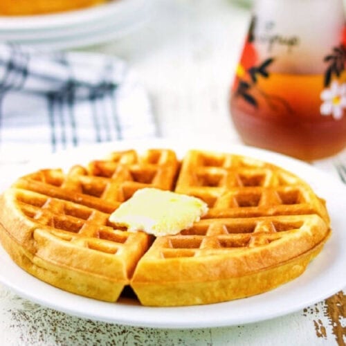 A crispy golden brown waffle on a white plate with a pat of butter melting on top.