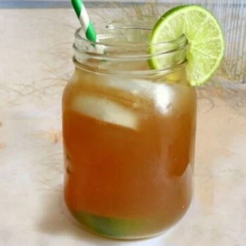 A closeup of a glass of Long Island Iced Tea on a beach.