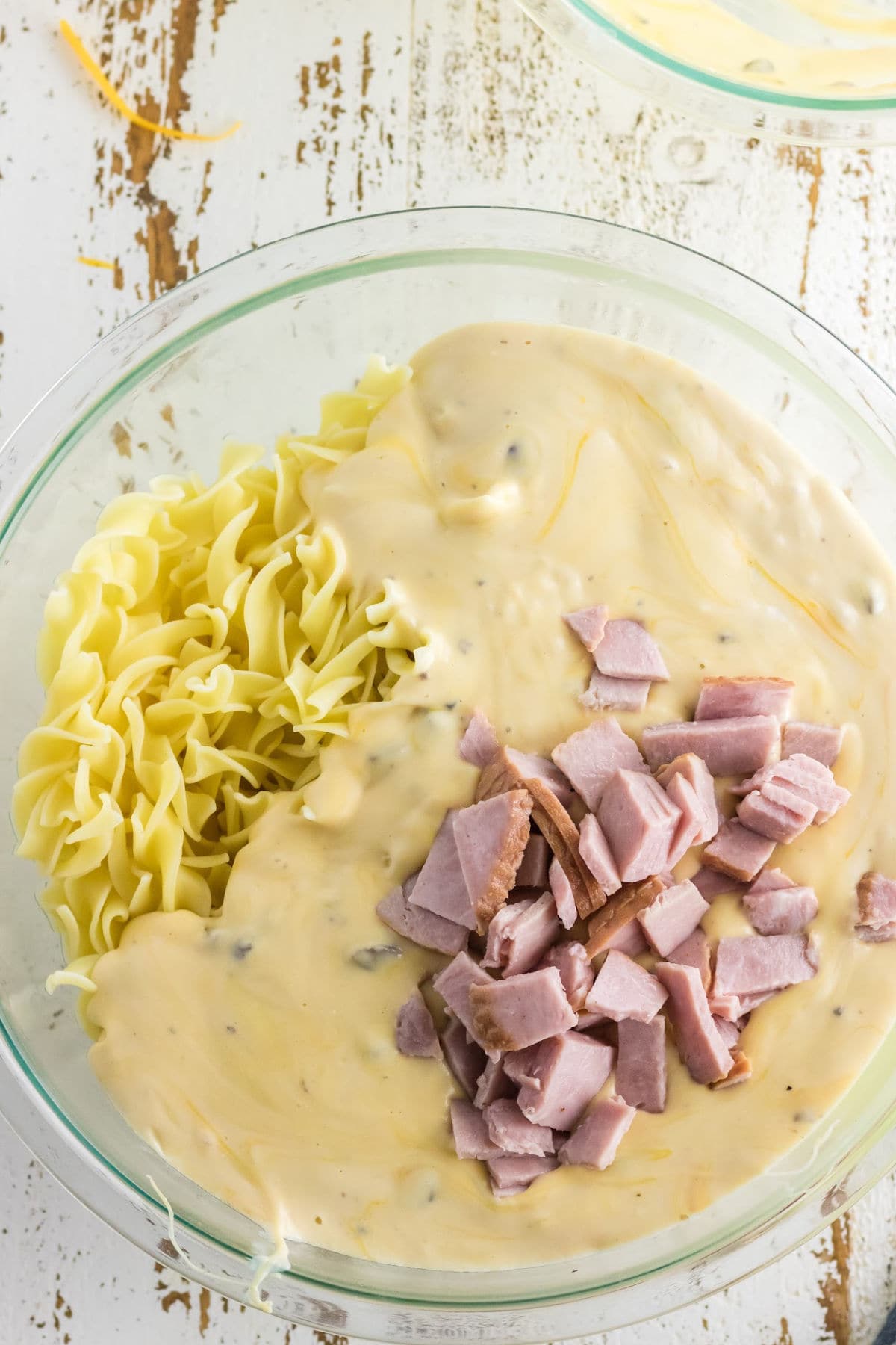Noodles and ham being stirred into sauce.