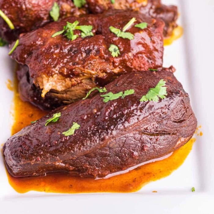 Closeup of finished Dr Pepper Country Style Ribs with a sticky sauce and a sprinkling of green parsley.