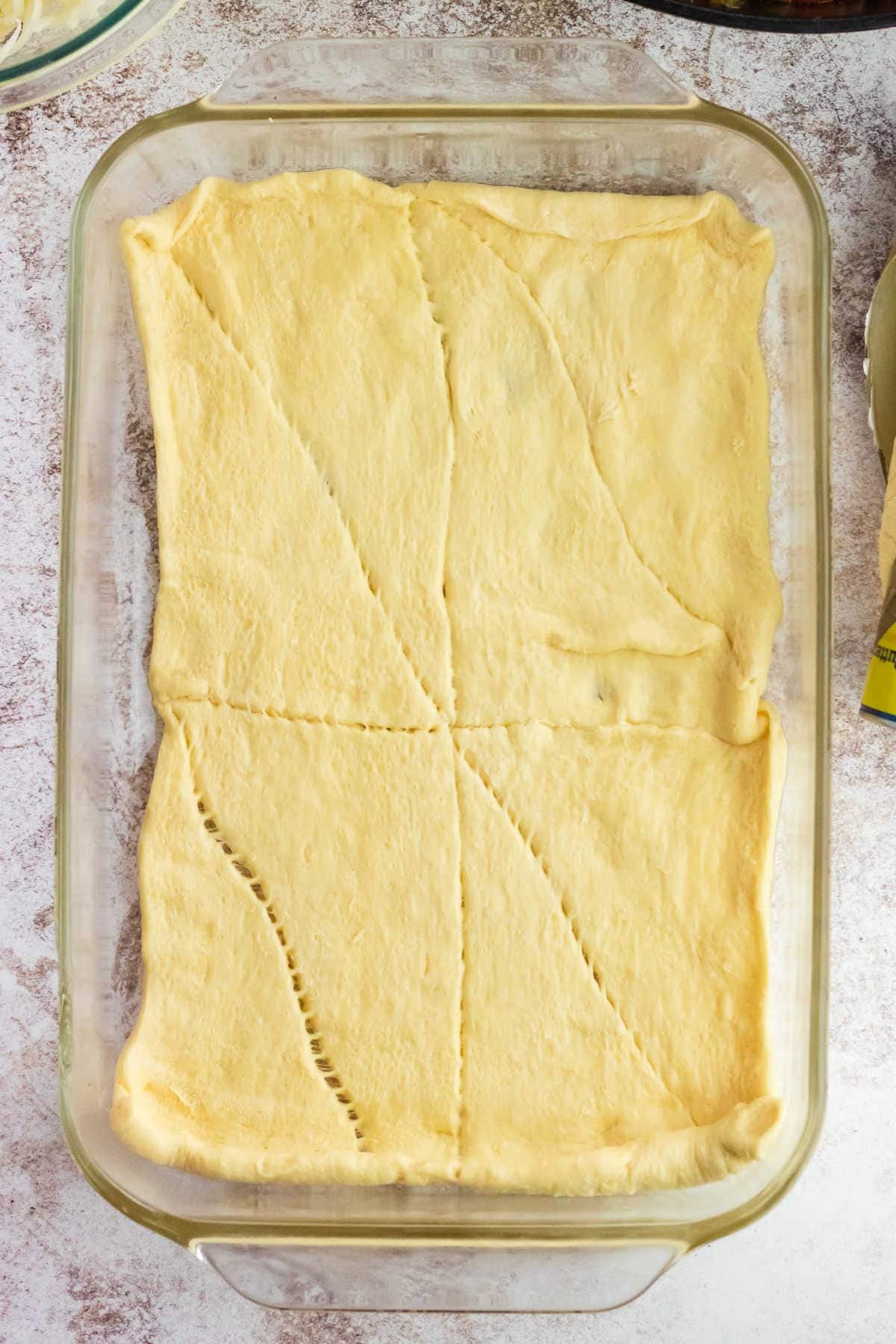 A layer of unbaked crescent roll dough on the bottom of the casserole dish.