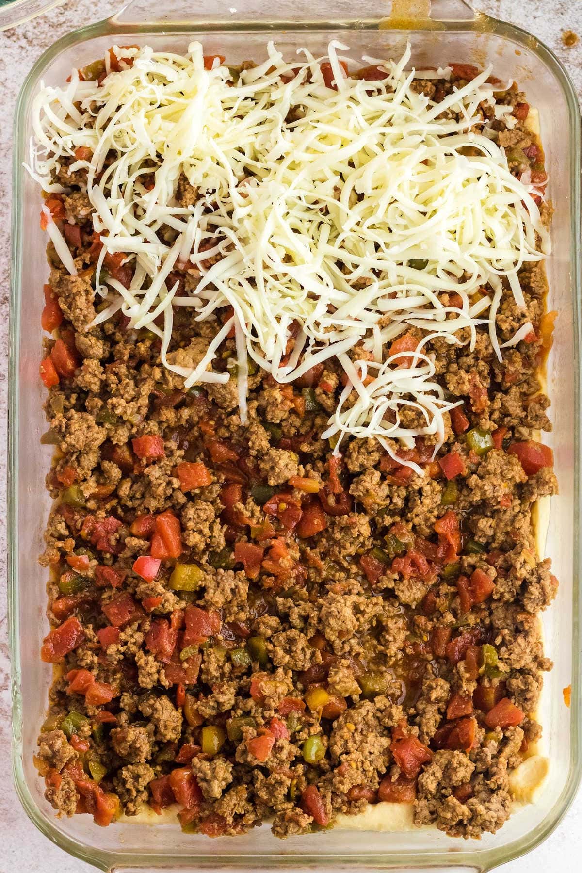 Layers of the cooked ground beef mixture and cheese over the crescent roll dough.