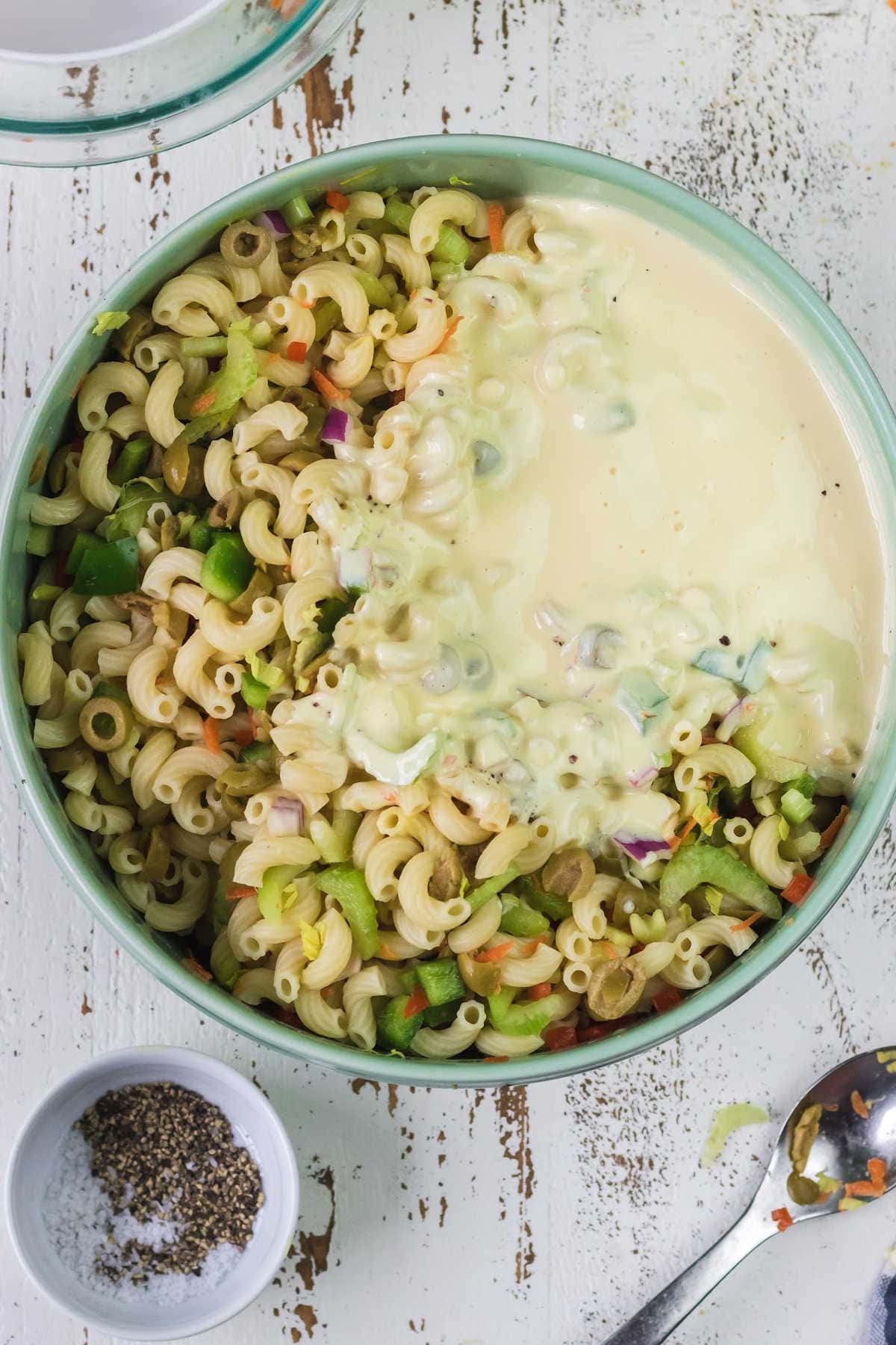 Dressing poured over macaroni salad ingredients.