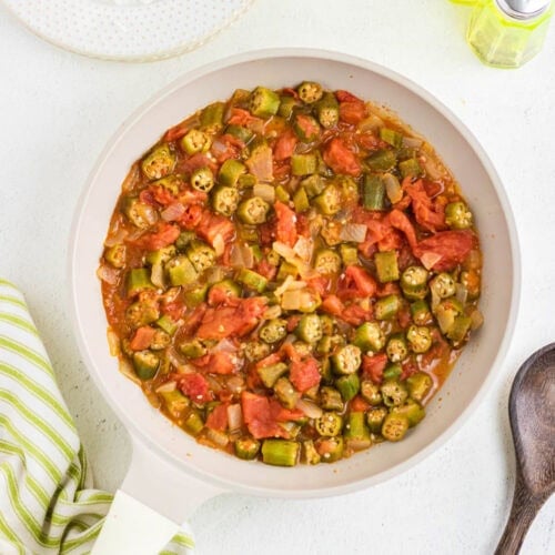 Overhead view of okra and tomatoes in a white pan.