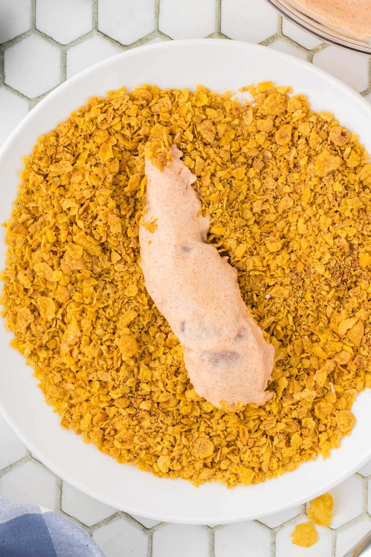 Chicken tenders being rolled in cornflakes.