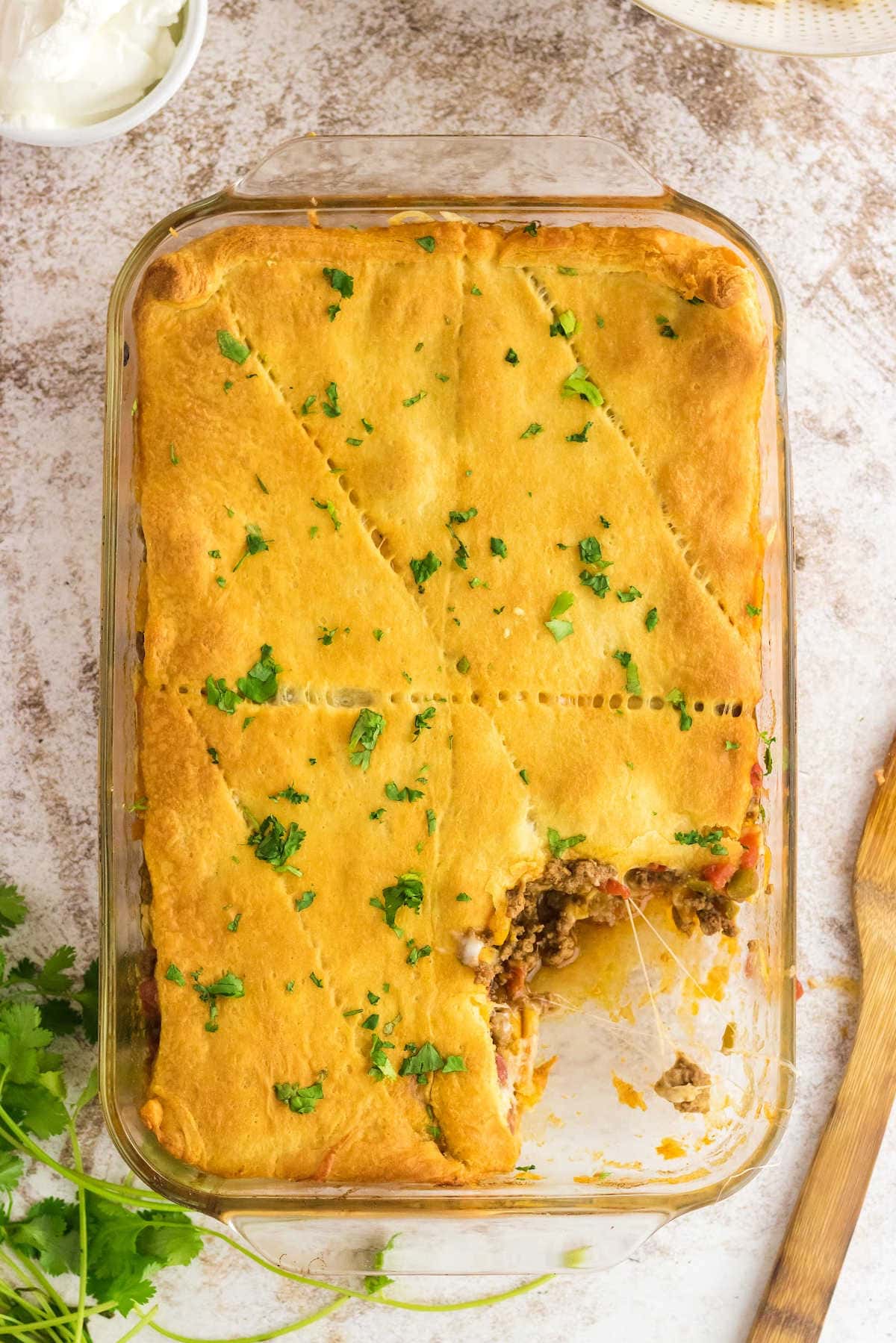 Overhead view of the golden top crust of the crescent roll taco bake with a serving removed showing the beefy filling.