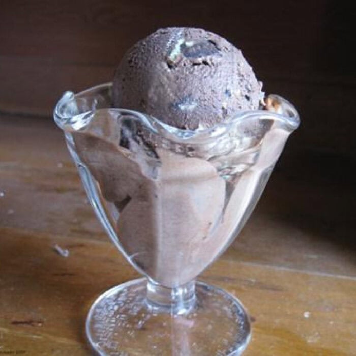 A scoop of chocolate Oreo ice cream in a glass ice cream dish.