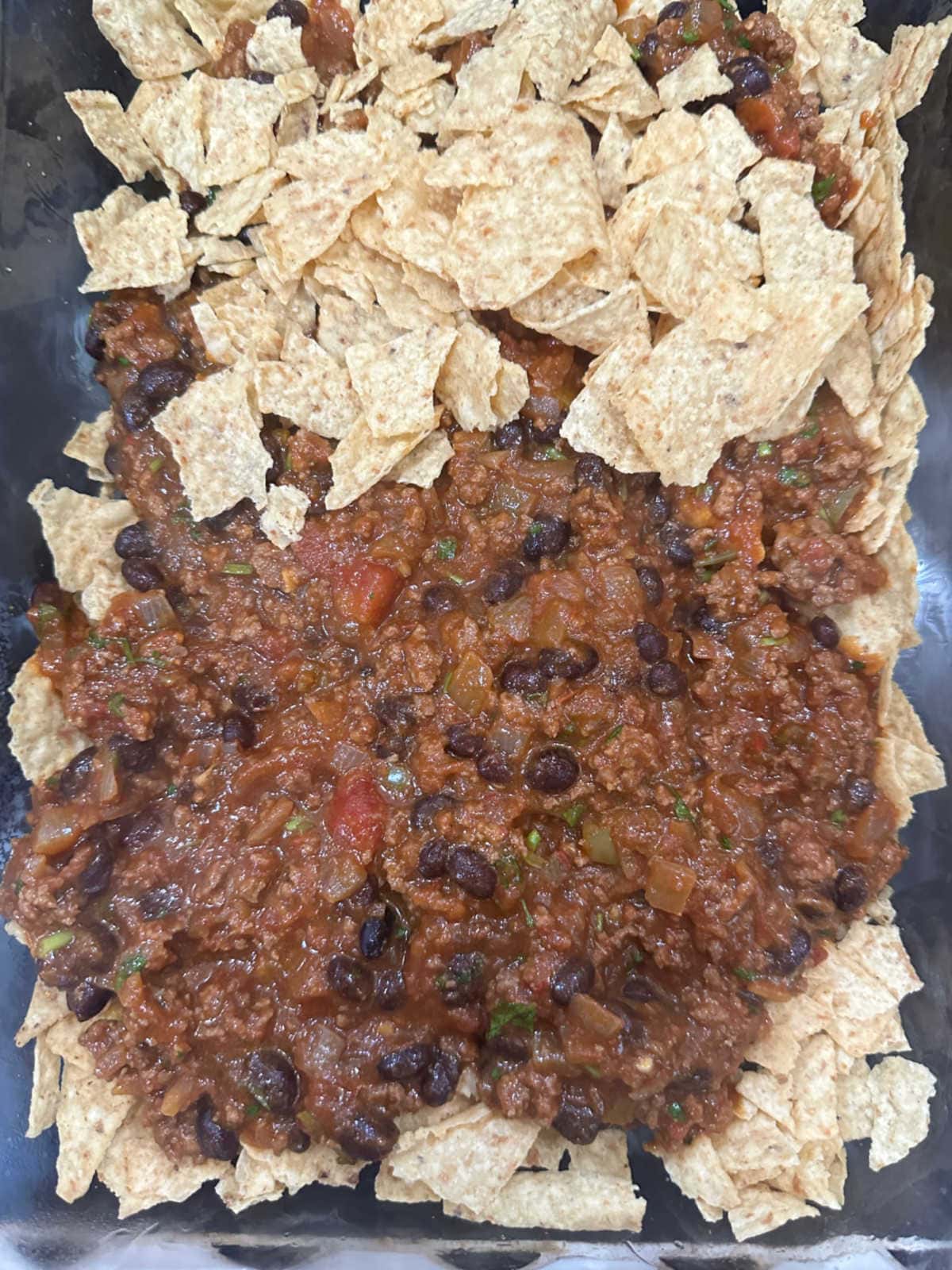 A layer of nacho chips and ground beef in a casserole dish.