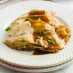 Closeup of slices of turkey breast covered in sauce on a white plate.