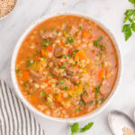 Overhead view of beef and barley soup in a white bowl.
