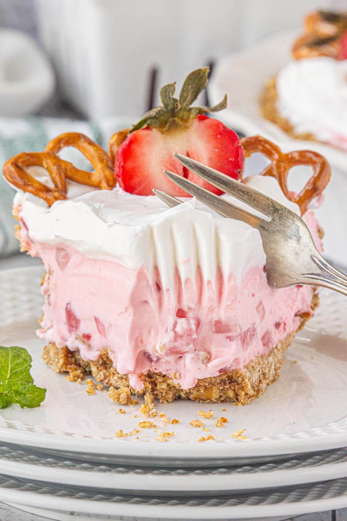A closeup of a slice of strawberry pretzel icebox pie being cut with a fork.
