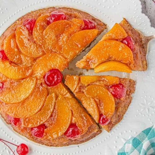 Peach Upside-Down Cake on a cake plate with a slice being removed.