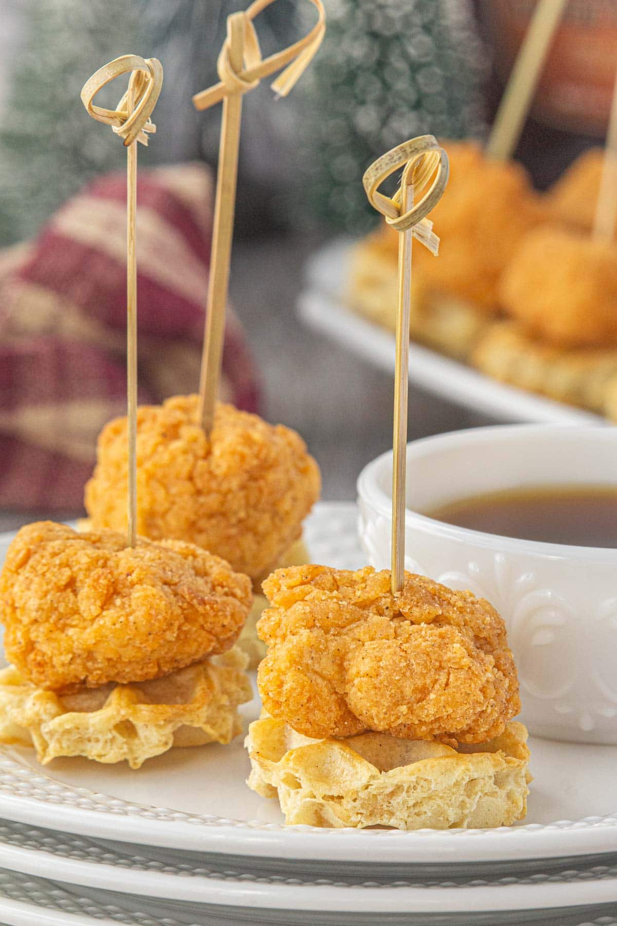Three mini chicken and waffles skewers on a serving plate.