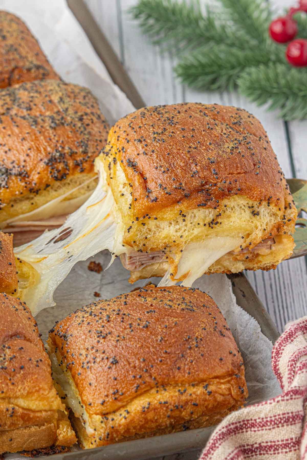 Hot ham and muenster cheese sliders with poppyseed butter glaze being removed from a cookie sheet.