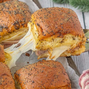 Baked ham and muenster sliders being removed from the baking sheet.