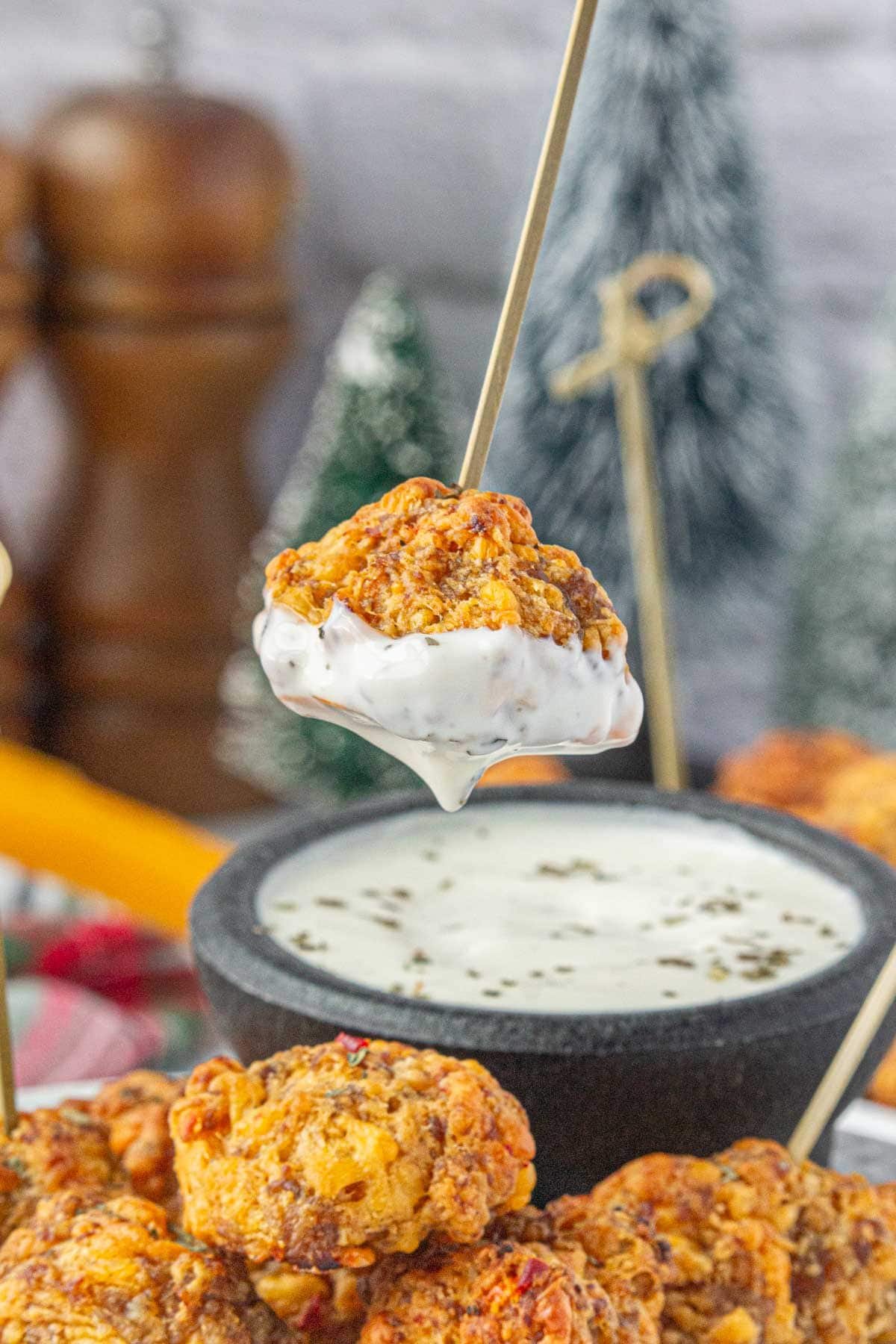 Pimento cheese sausage ball appetizer on a skewer being dipped in jalapeno ranch dip.