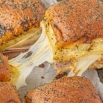 Sliders being pulled off a cookie sheet with gooey cheese. Text overlay for Pinterest.