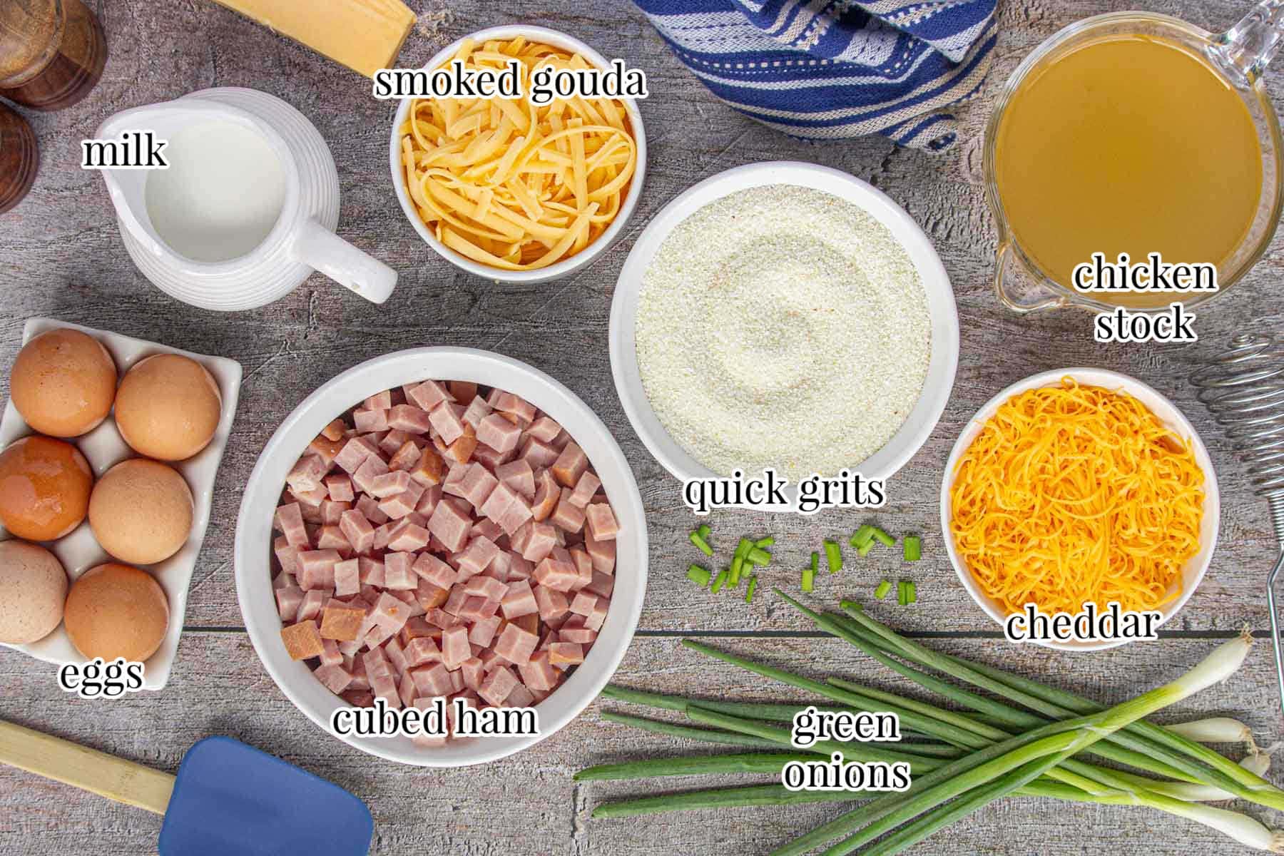 Labeled ingredients for ham and cheese grits casserole include smoked gouda cheese, cheddar, ham, quick grits, chicken stock, eggs, milk, and green onions.