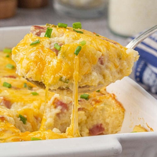 Closeup of ham and cheese breakfast bake being served from a white casserole dish.