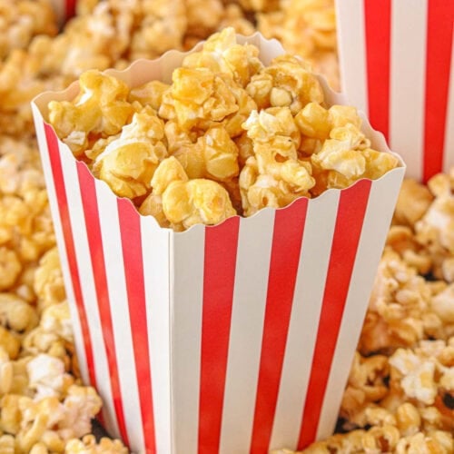 Overhead view of homemade caramel popcorn in a red and white striped box.